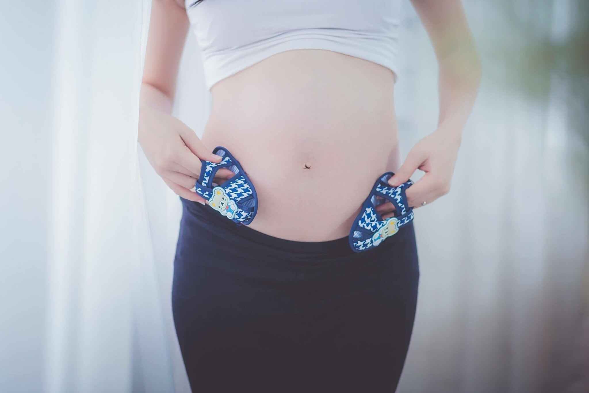 pregnant mom to be in athleisure wear carrying 2 baby shoes